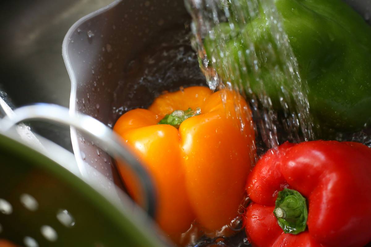 Close-up of hands scrubbing a muddy potato under running water, demonstrating how to clean a potato properly before peeling